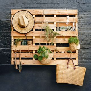 Garden wooden pallet storage on wall with hat, bag, garden tools and hanging planters and plants