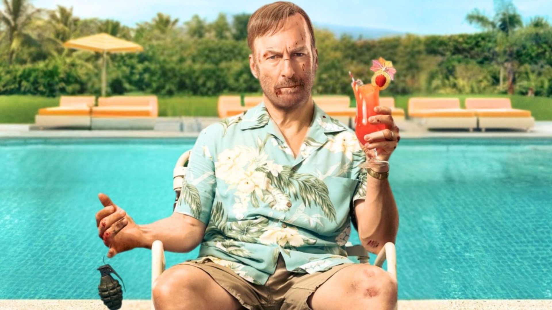 Bob Odenkirk sits by a pool holding a cocktail in one hand and a grenade in the other