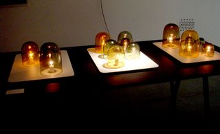 Three trays on a table with glass candle holders each covering a light bulb.
