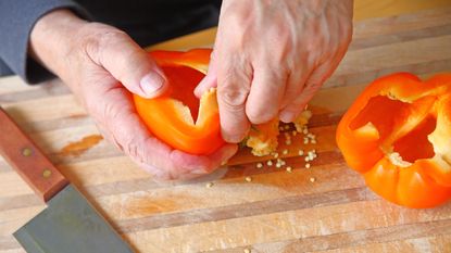 Male hands remove seeds from an orange bell pepper on a cutting board