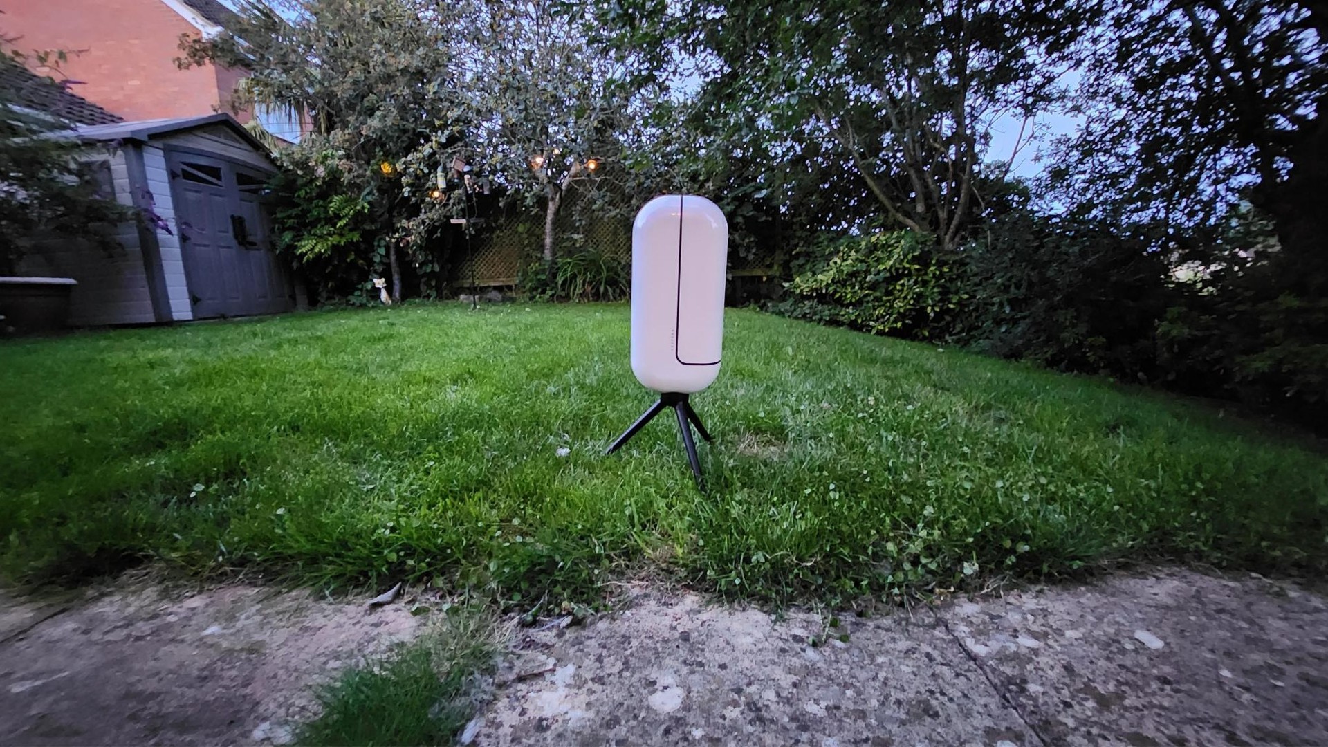 Image of the Vaonis Vespera Observation Station. It's a sleek white capsule balanced on a black tripod in a garden. The telescope/camera arm is closed at the moment.