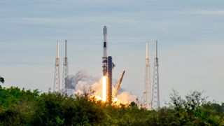 a white rocket lifts off above a plume of fire