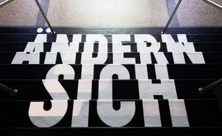 Looking down a short staircase painted black with white text reading "ANDERN SICH"