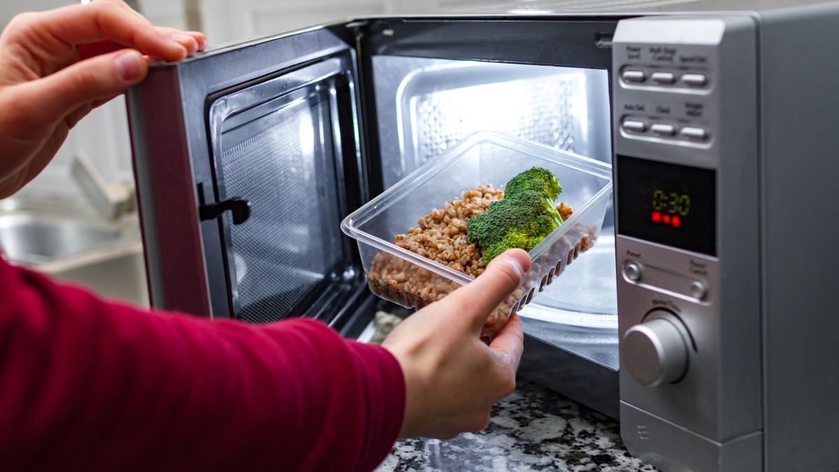 A plastic container filled with food being put in a microwave