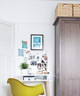 Yellow Eames style chair in front of white desk next to wooden wardrobe, study area in bedroom.