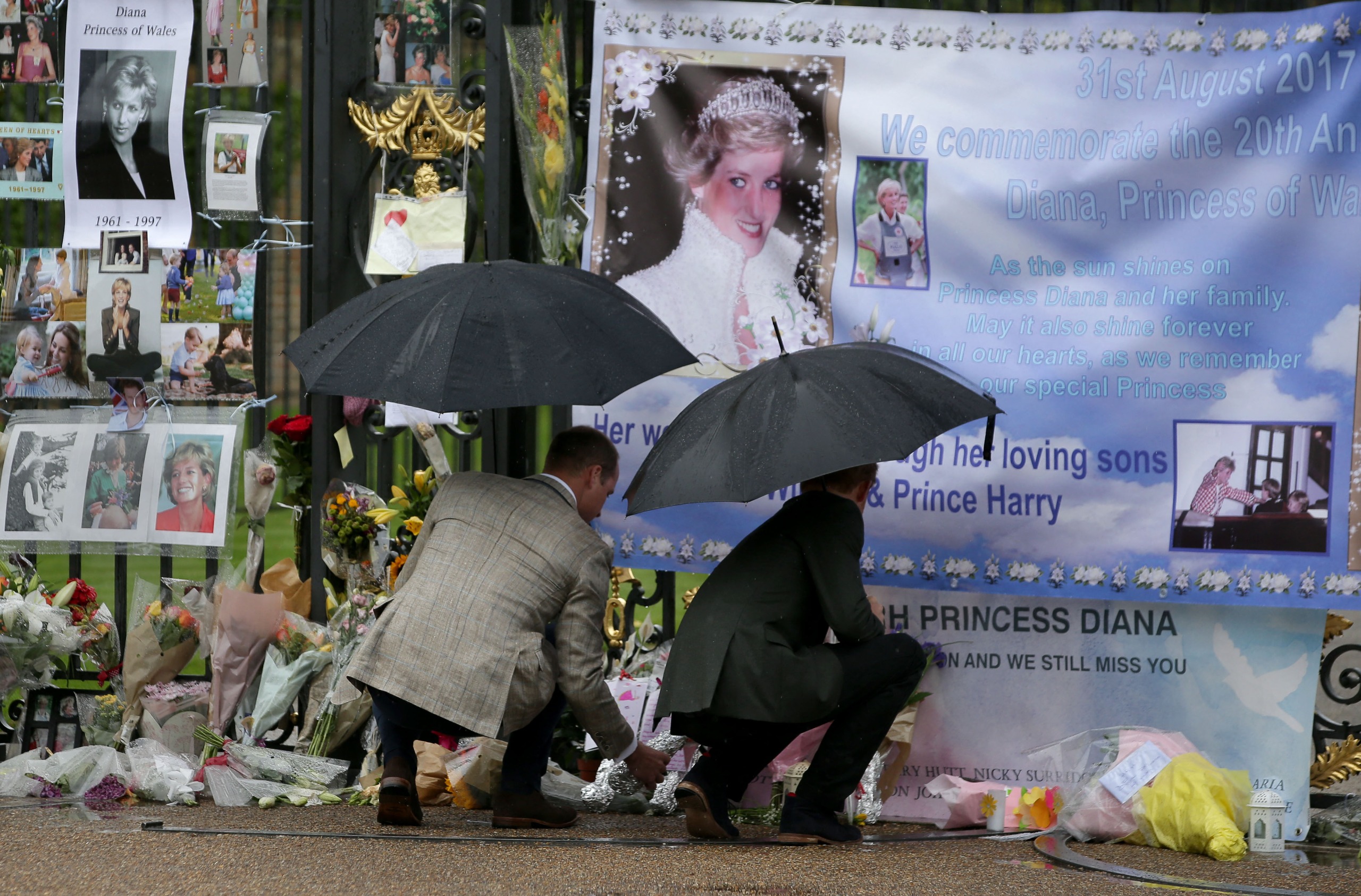 Prince Harry and Prince William holding umbrellas looking at tributes to Princess Diana