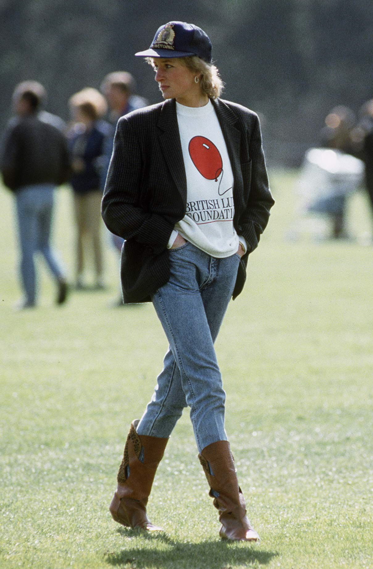 Diana, Princess of Wales at Guards Polo Club. She is wearing a sweatshirt with the British Lung Foundation logo on the front, jeans, boots, and a baseball cap.