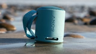 Sony SRS-XB100 Bluetooth speaker on sand at beach with water in background