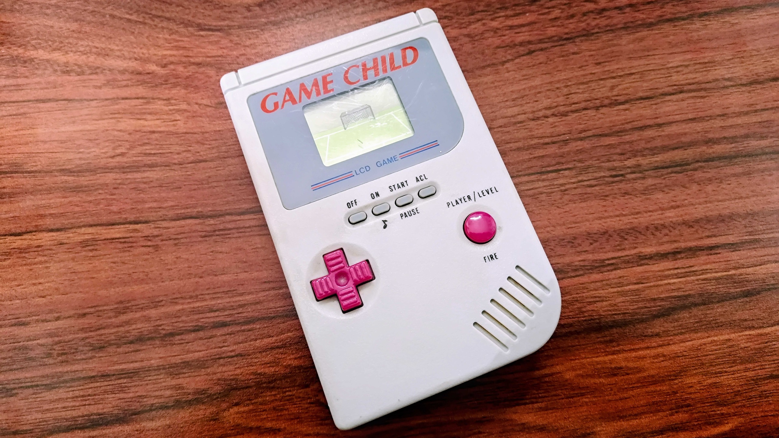 Game Child LCD Game Boy clone on woodgrain desk.