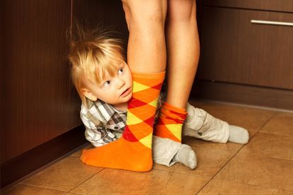 Shy boy hiding behind mother's legs.