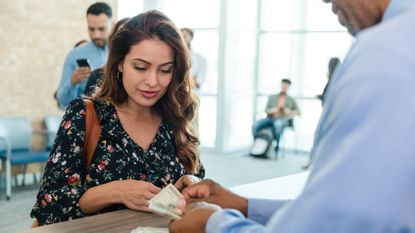 Woman standing at a bank counter as the teller counts out cash to hand her