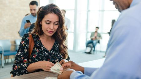 Woman standing at a bank counter as the teller counts out cash to hand her