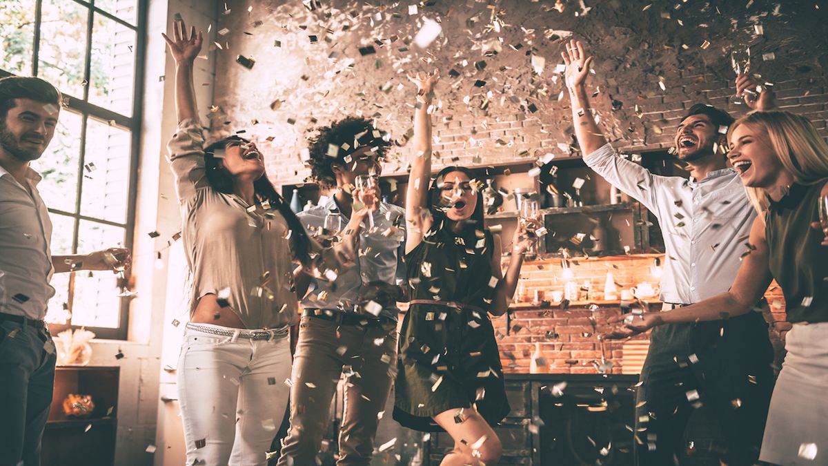 A group of people jump into the air with arms raised as confetti rains down.