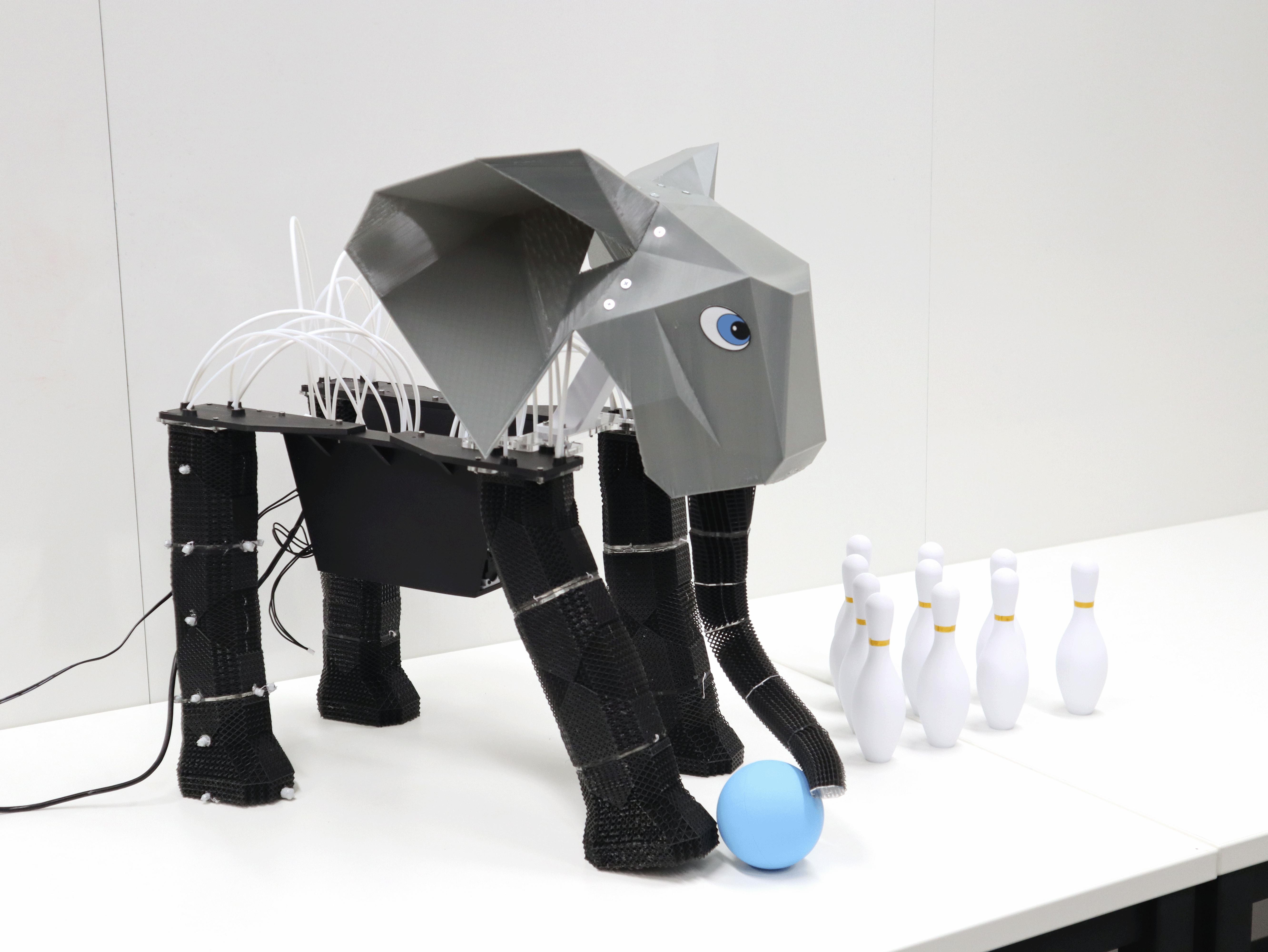 A photograph of a robot elephant with a blue ball, standing next to bowling pins.