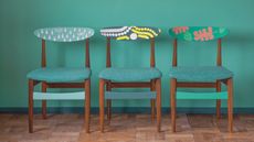 Three mid-century dining chairs with green Chalk Paint details and patterns and green upholstery in front of green wall