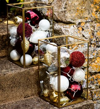 Brass and glass lanterns filled with red gold and white baubles on doorstep