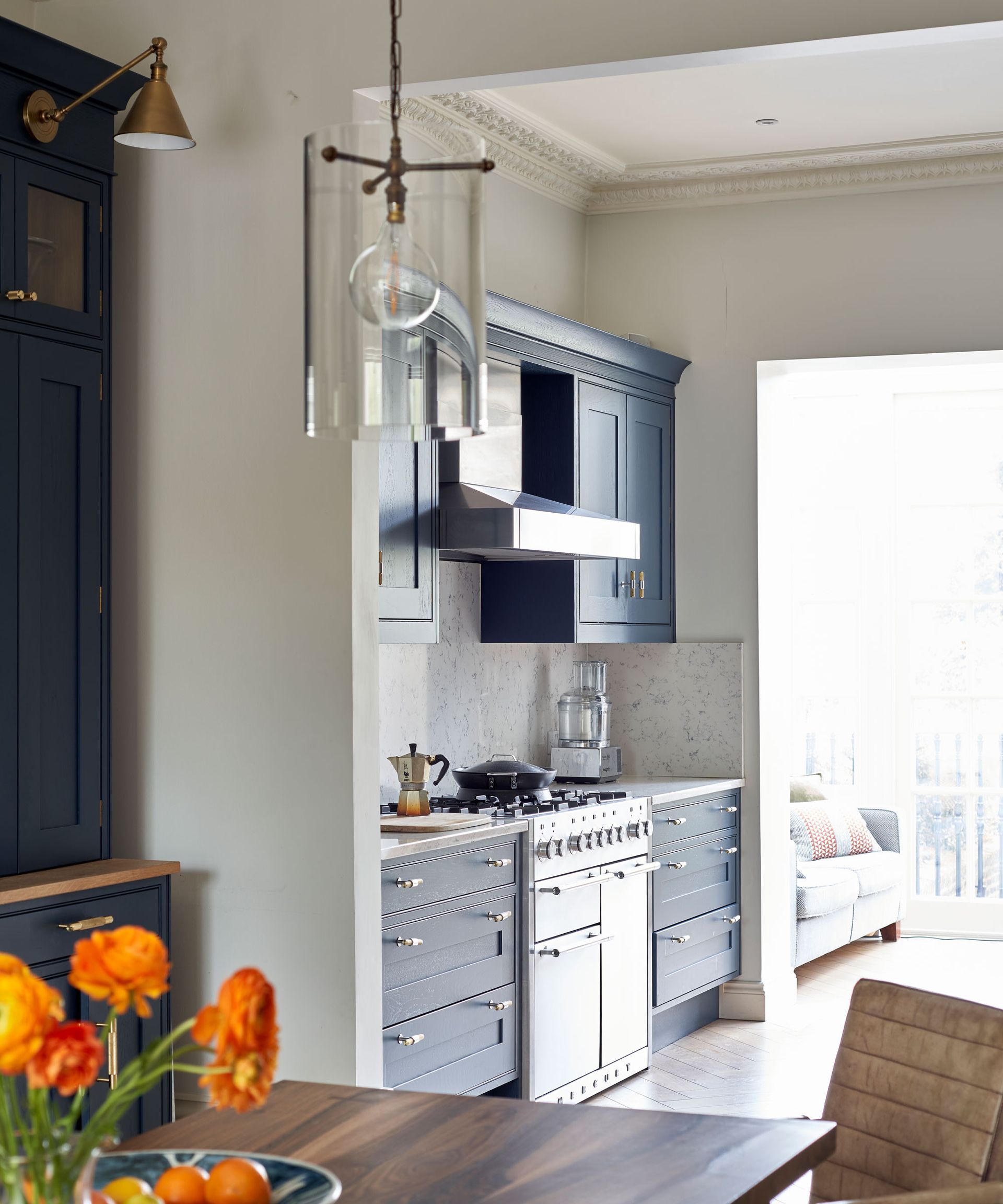 Close up of glass pendant over dining table, kitchen in background, blue cabinetry, flowers and fruit on table