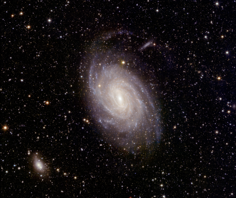 En el centro de esta imagen espacial se ve una magnífica galaxia espiral.  Al fondo hay muchas estrellas.  Hacia la parte inferior izquierda de la escena hay una mancha blanca brumosa mucho más pequeña.