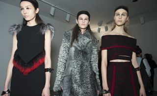 3 models wearing black dress with maroon and grey fur trim, grey fur coat and black dress with maroon trim