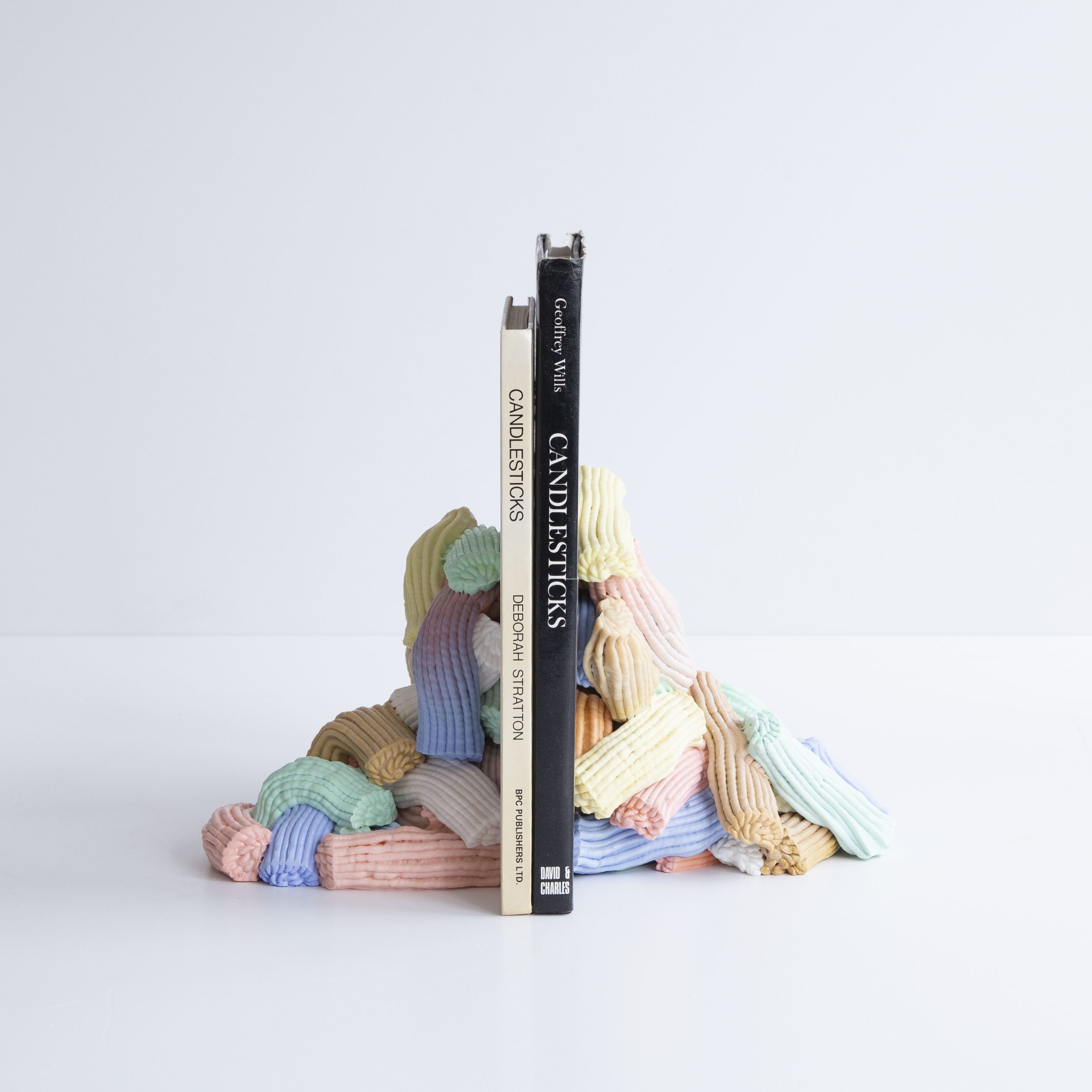 A book stand made from pastel-shaded, icing-looking material holds a beige and a black book in an all-white room.