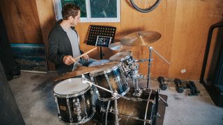 Man plays drums in his garage with Drumeo running on a tablet to his left