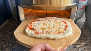 Cheese pizza on pizza peel in front of Solo Stove Pi Prime pizza oven