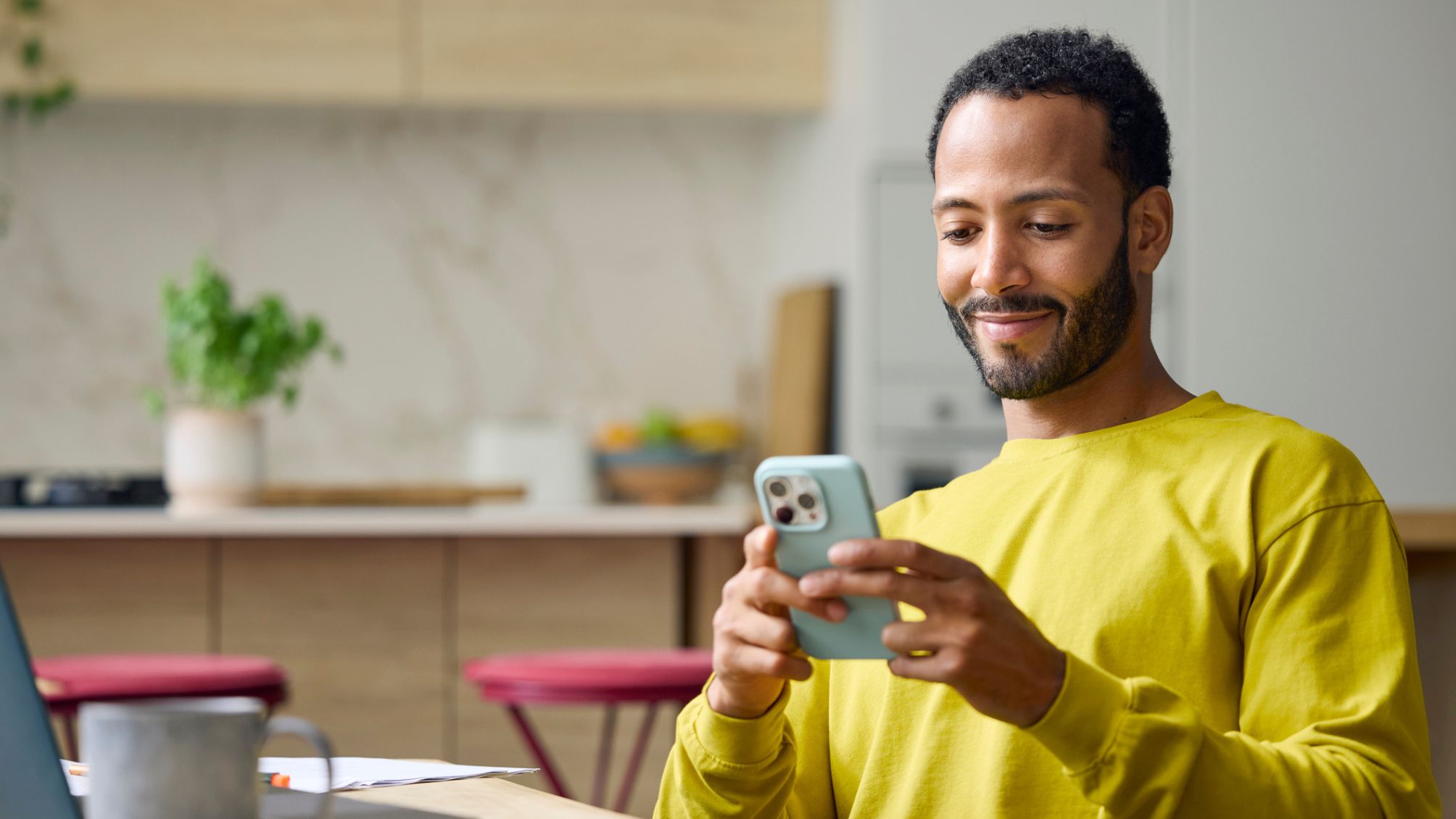 A man smiling, using his smartphone at home.