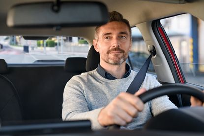 Smiling mature businessman with seat belt on driving vehicle