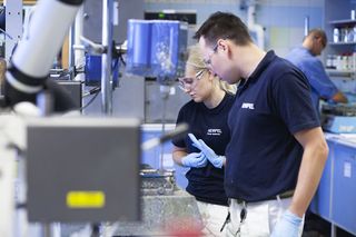 A photo of two workers inside a factory wearing blue uniforms displaying the Hempel logo