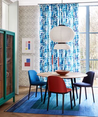 Dining room with blue curtains and rug, grey wallpaper and wall art, wooden flooring and lantern pendant light