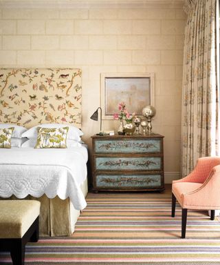 Eclectic bedroom with bird inspired headboard, ornate painted chest of drawers, artwork, metallic objet, and multi color striped carpet.