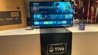TiVo OS running on a 55-inch TV sitting on a table with a white tablecloth