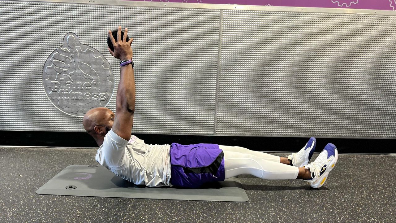 Teddy Savage performing a dumbbell hollow hold with flutter kicks