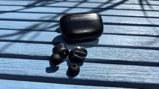 Bowers & Wilkins Pi8 wireless earbuds out of their case, placed on a blue table