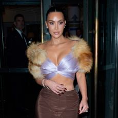 Kim Kardashian wearing a sleek updo hairstyle. She is wearing a top that has fur sleeves and a purple bralette.