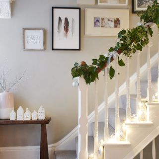 Grey and white hallway with white bannisters decorated with christmas garland and fairy lights