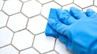Hand with blue rubber glove cleaning hexagonal tiles with a blue sponge