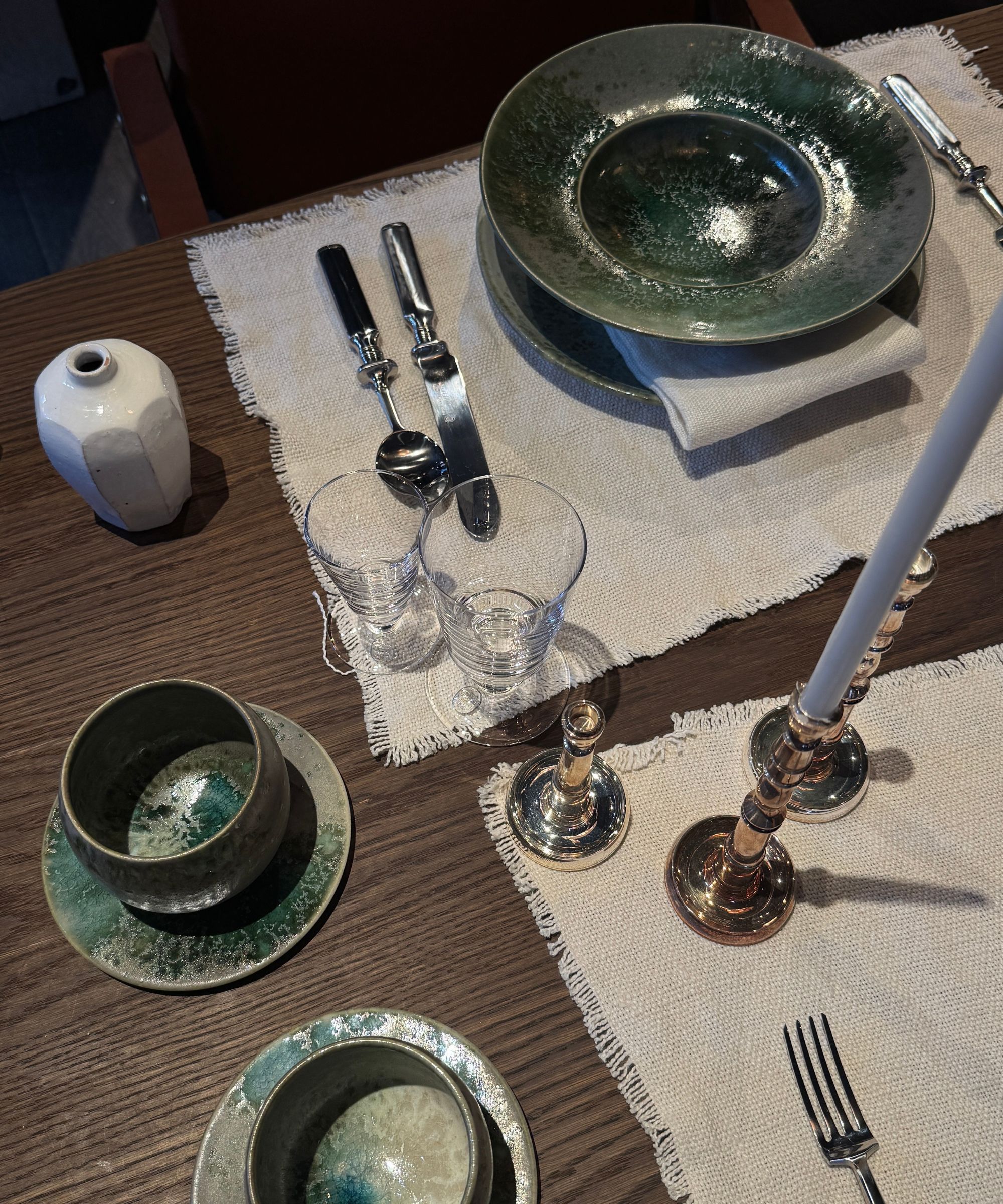 a table set with green reactive dinnerware, linen placemats, silver candlesticks, glassware, and silver cutlery
