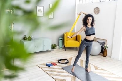 Young woman looking away while exercising with resistance band and yoga accessories at home