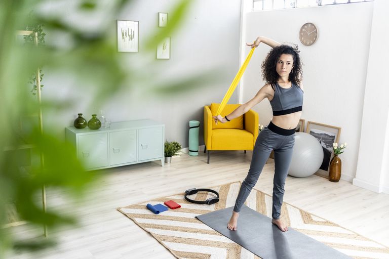 Young woman looking away while exercising with resistance band and yoga accessories at home
