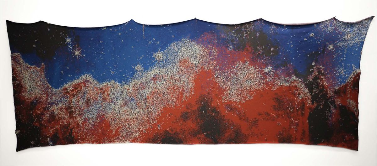 Un tapiz tejido se sienta en una pared blanca, que representa la nebulosa carina