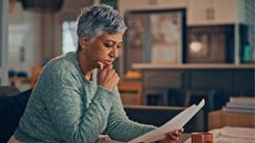An older woman looks thoughtful as she looks over paperwork in her home office.