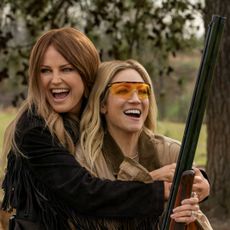 Malin Akerman as Margo hugging brittany snow as sophie from behind and showing her how to shoot a riffle in the tv show hunting wives