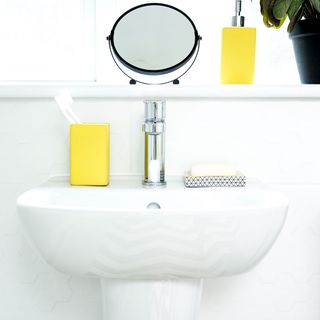 basin with silver coloured tap and yellow coloured toothbrush holder