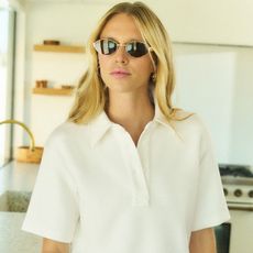 A blonde model searing sunglasses poses in a white button-down short-sleeve shirt and sunglasses.