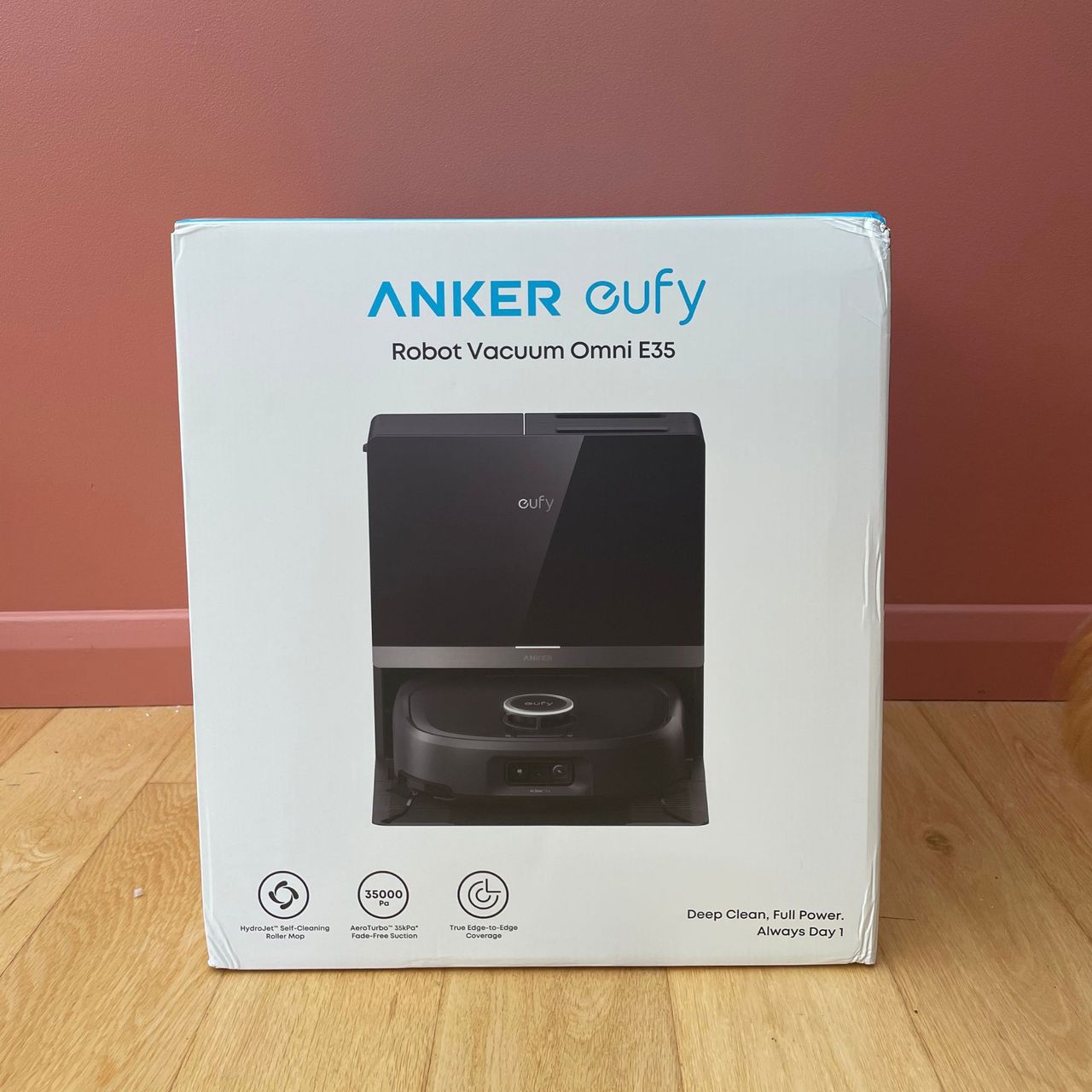 Anker eufy Robot Vacuum E35 Omni box sitting on wood flooring, in front of a paint painted wall
