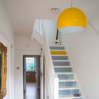 hallway with blue painted stairs and bright yellow pendant light