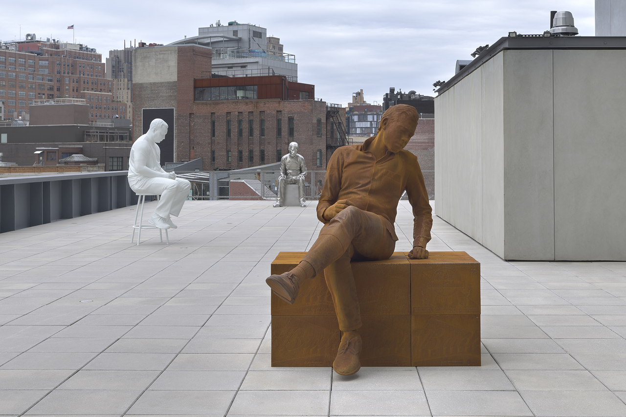 A roof terrace display 3 sculptures of large metal men - one is rusted, another painted silver and another in white.