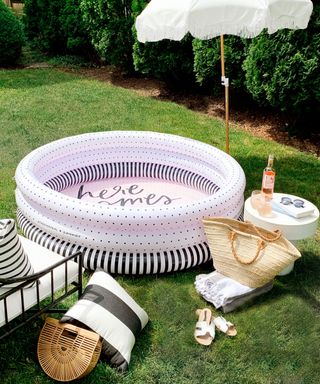 A Minnidip branded inflatable paddling pool with parasol, women's handbag, white flat sandals on grass in backyard