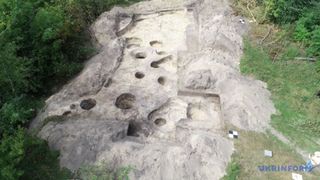 Photo of an archaeological site in Ukraine that dates to the Scythian period; the outline of a structure can be seen in stone with several indentations in the floor